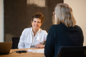 Ärztin bespricht mit Patientin am Holztisch im Sprechstundenzimmer